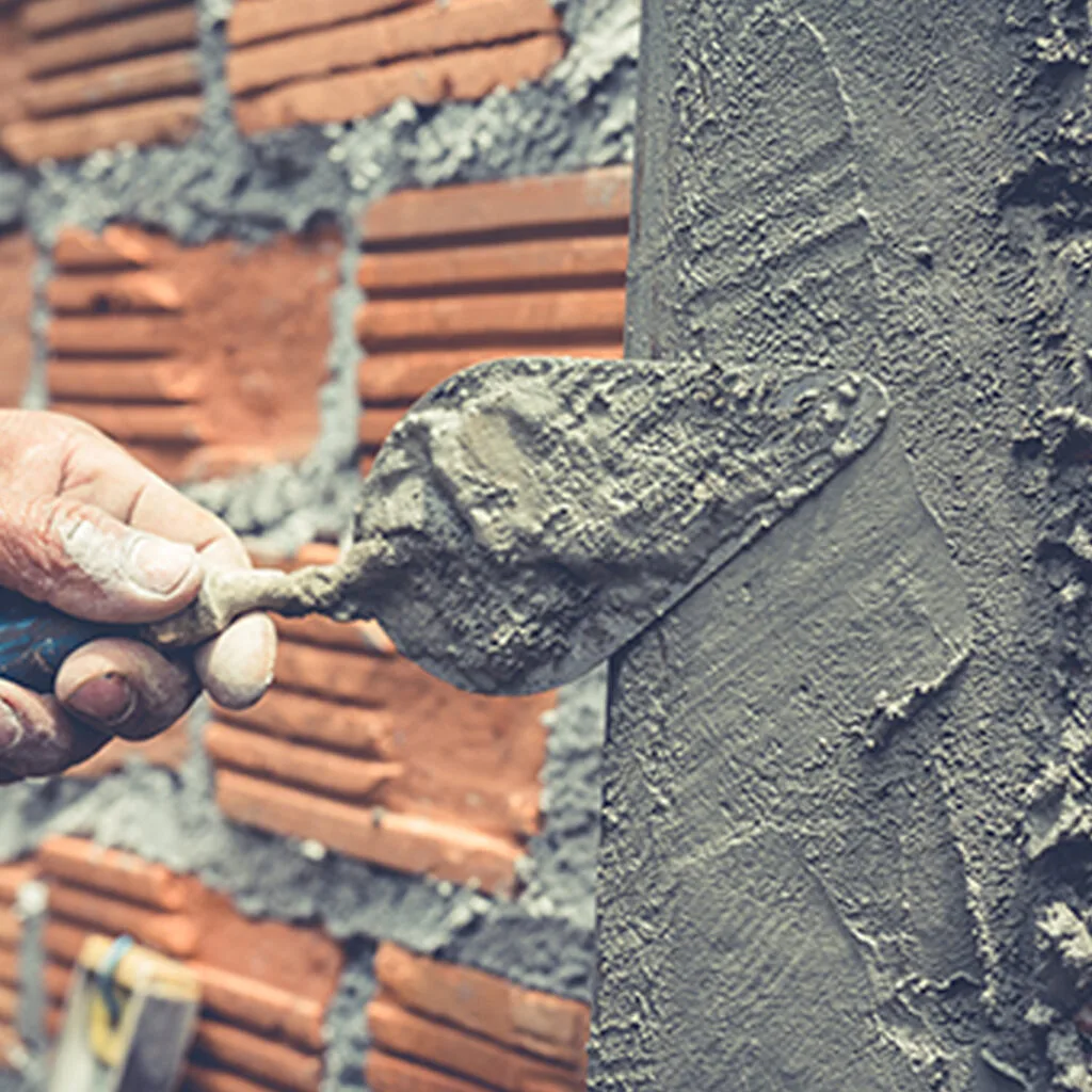 Close-up of a mason applying fresh cement to a brick wall with a trowel, ideal for masonry contractors near me offering repair services.