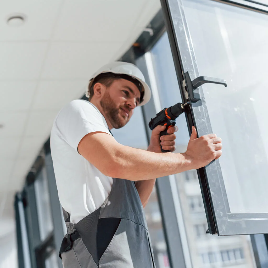 Contractor using a drill to install a glass window frame in a residential setting for home window repair near me services.