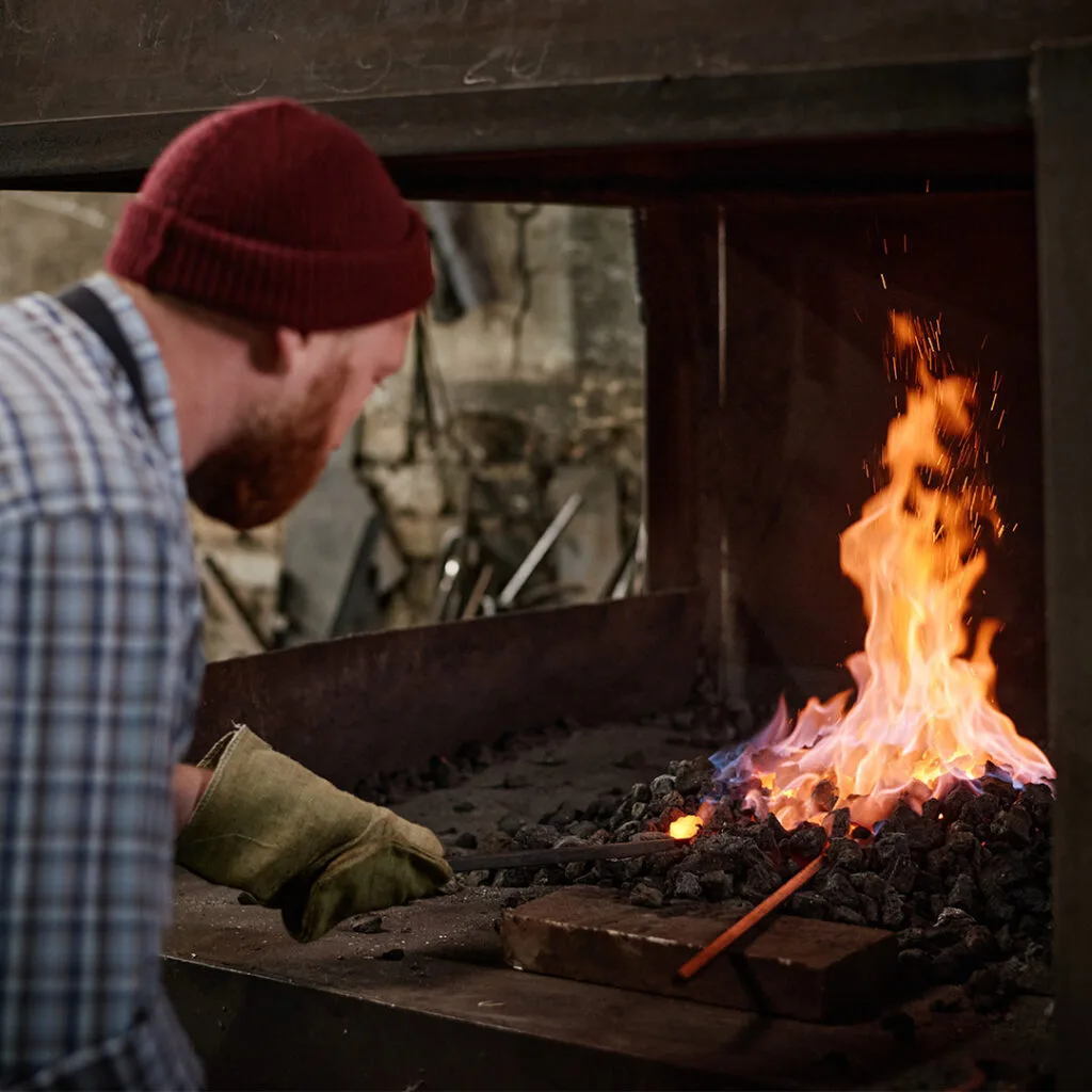 Worker tending to a hot forge fire, relevant to traditional fireplace maintenance but not typical of a chimney sweep near me service.
