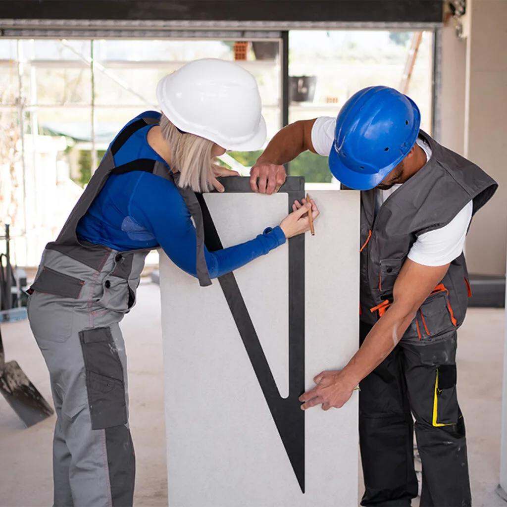 Two contractors in hard hats measuring a drywall panel on-site, preparing for drywall repair near me service.