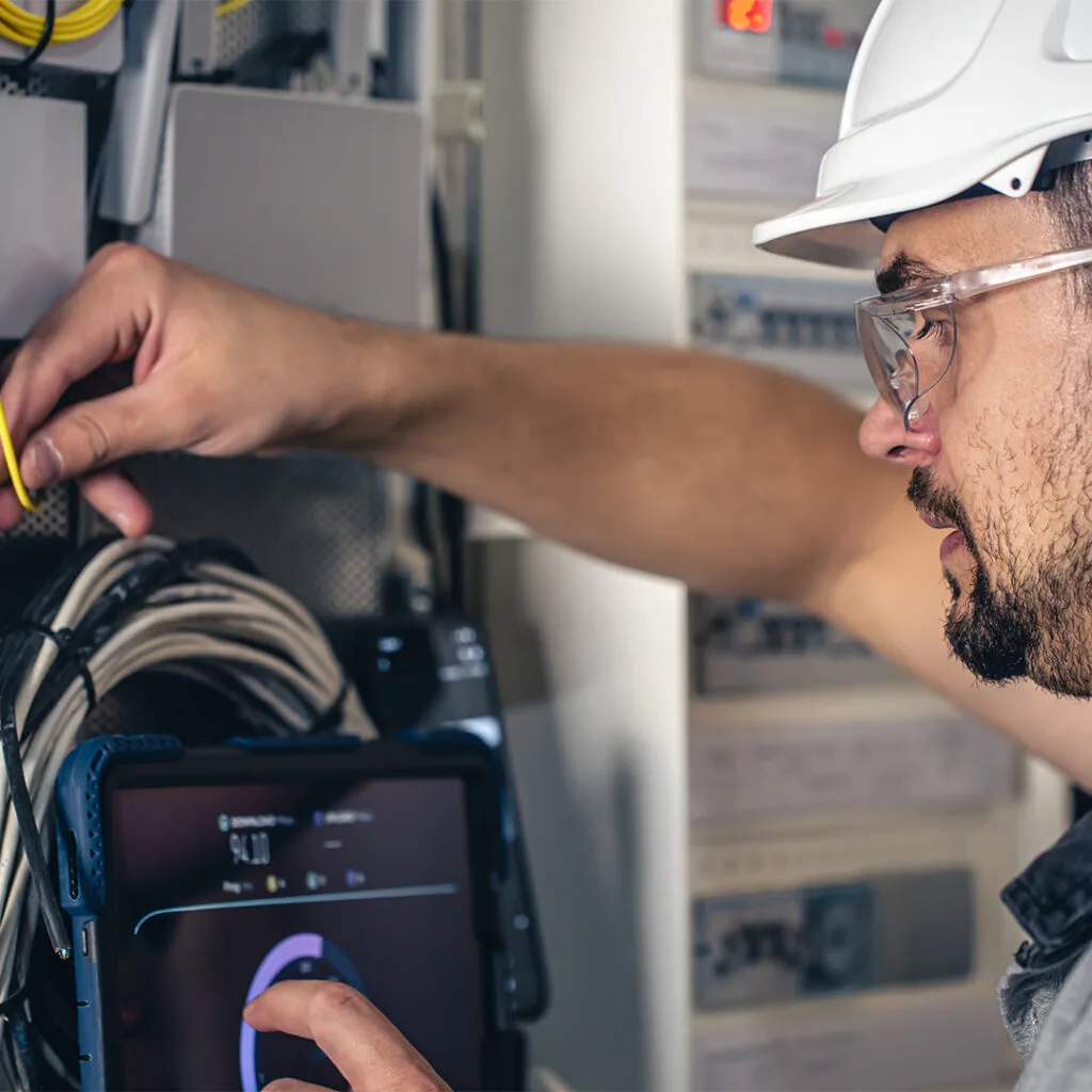 Electrical handyman near me inspecting a control panel and monitoring system diagnostics using a touchscreen device.