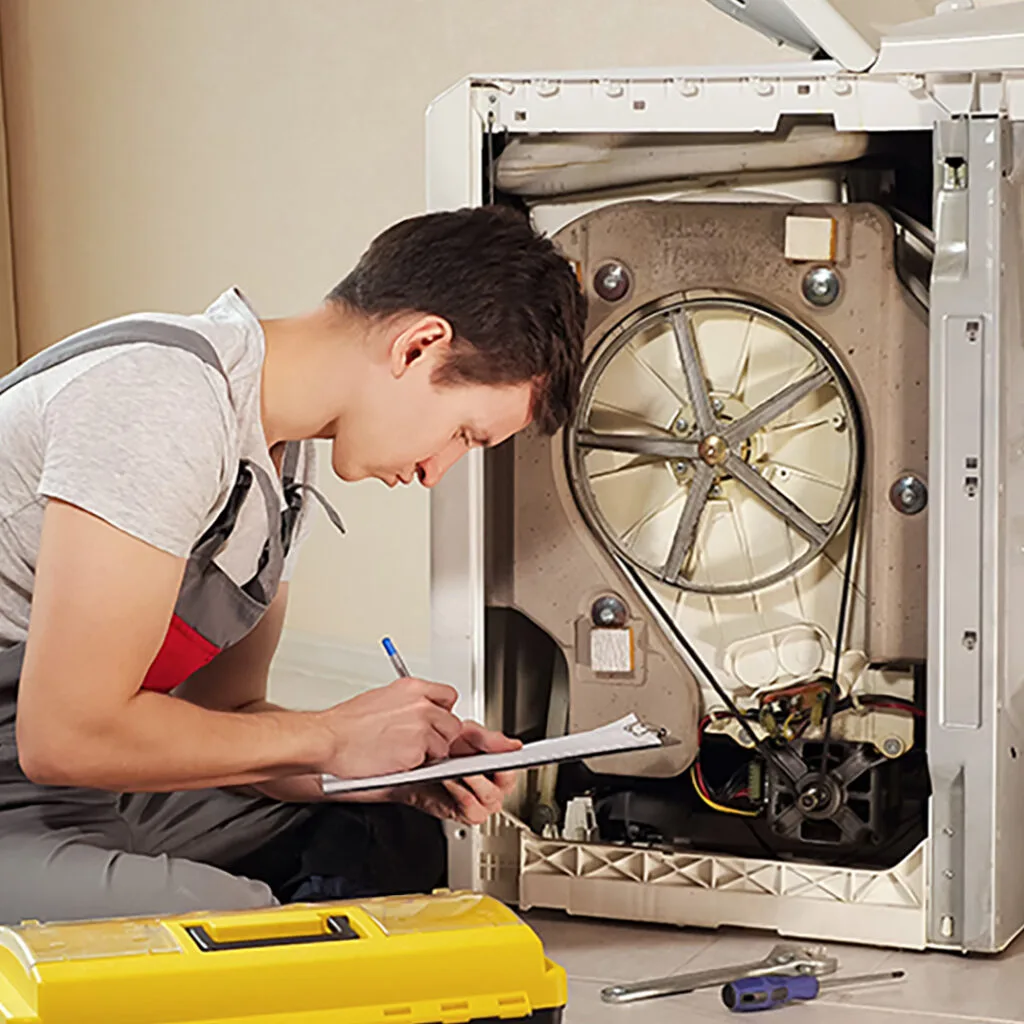 Technician inspecting a washing machine motor and taking notes during an affordable appliance repair service.