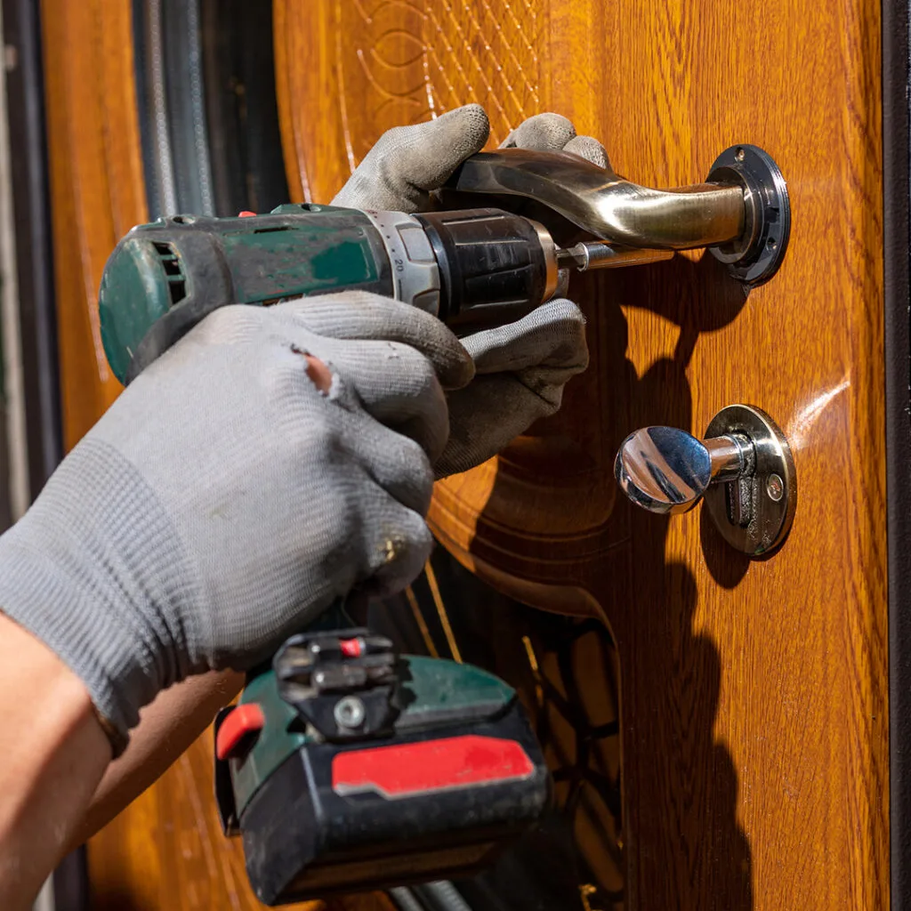 Gloved hands using a power drill to install a door handle, illustrating emergency locksmith near me services.