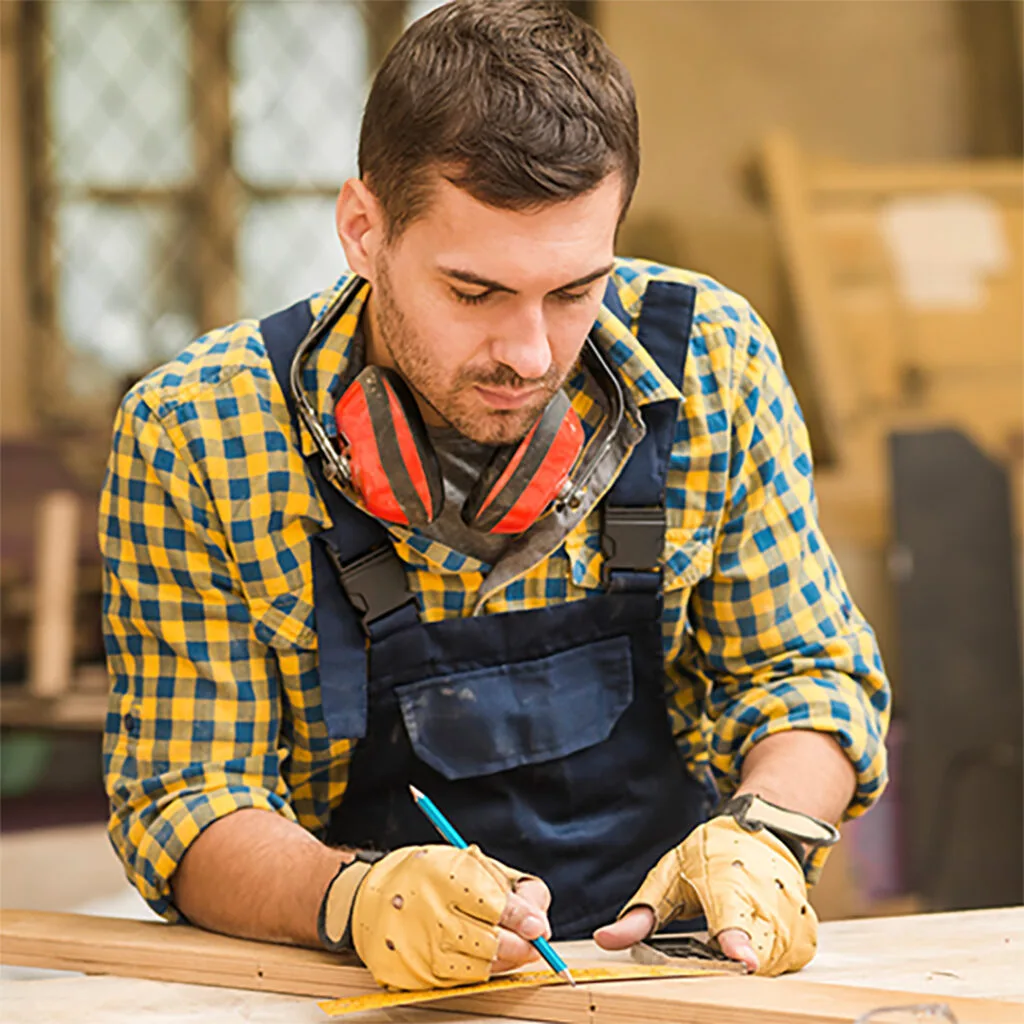 Carpenter near me measuring and marking a wooden board in a workshop while preparing for a custom woodworking project.