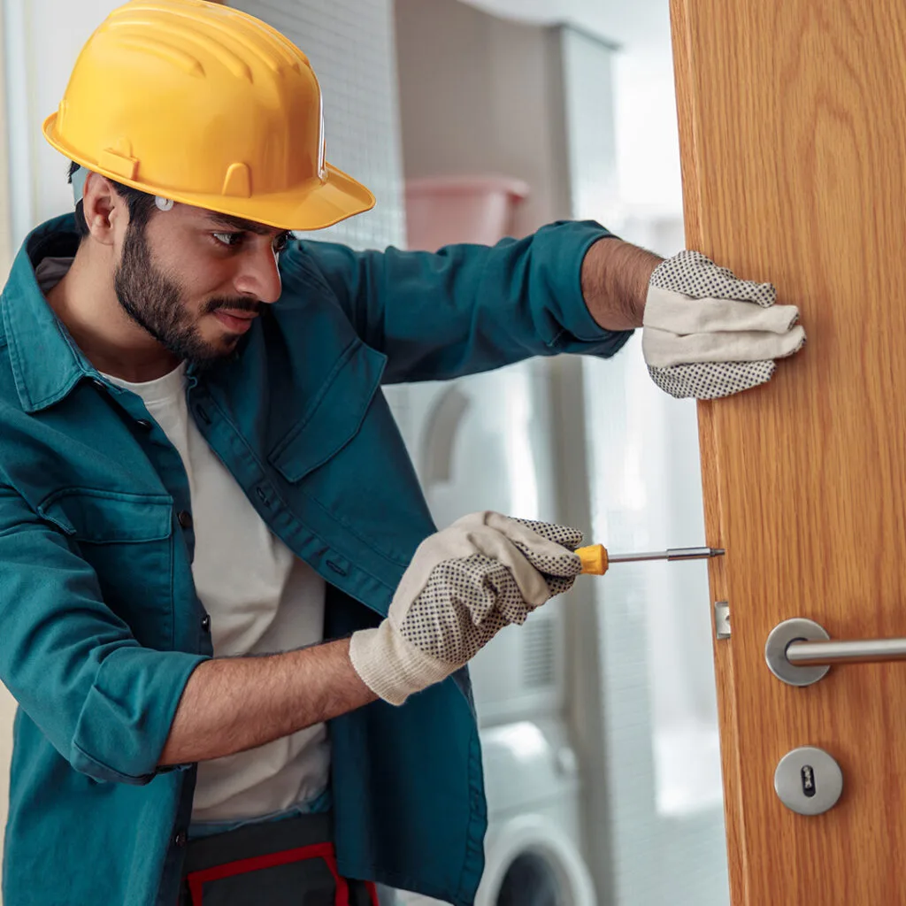 Technician in safety gear installing a door handle with a screwdriver during a door installation near me service.