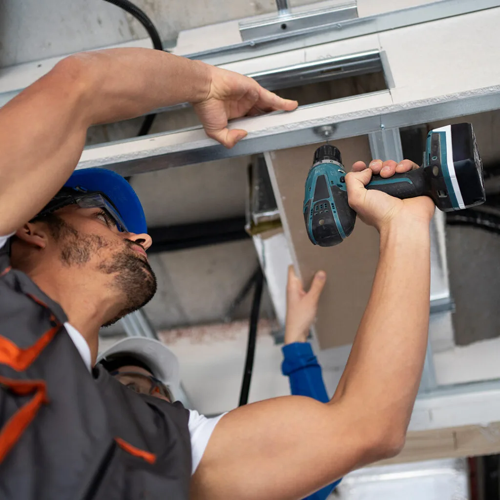 Technician securing a metal garage door track with a power drill during garage door service and repair near me.
