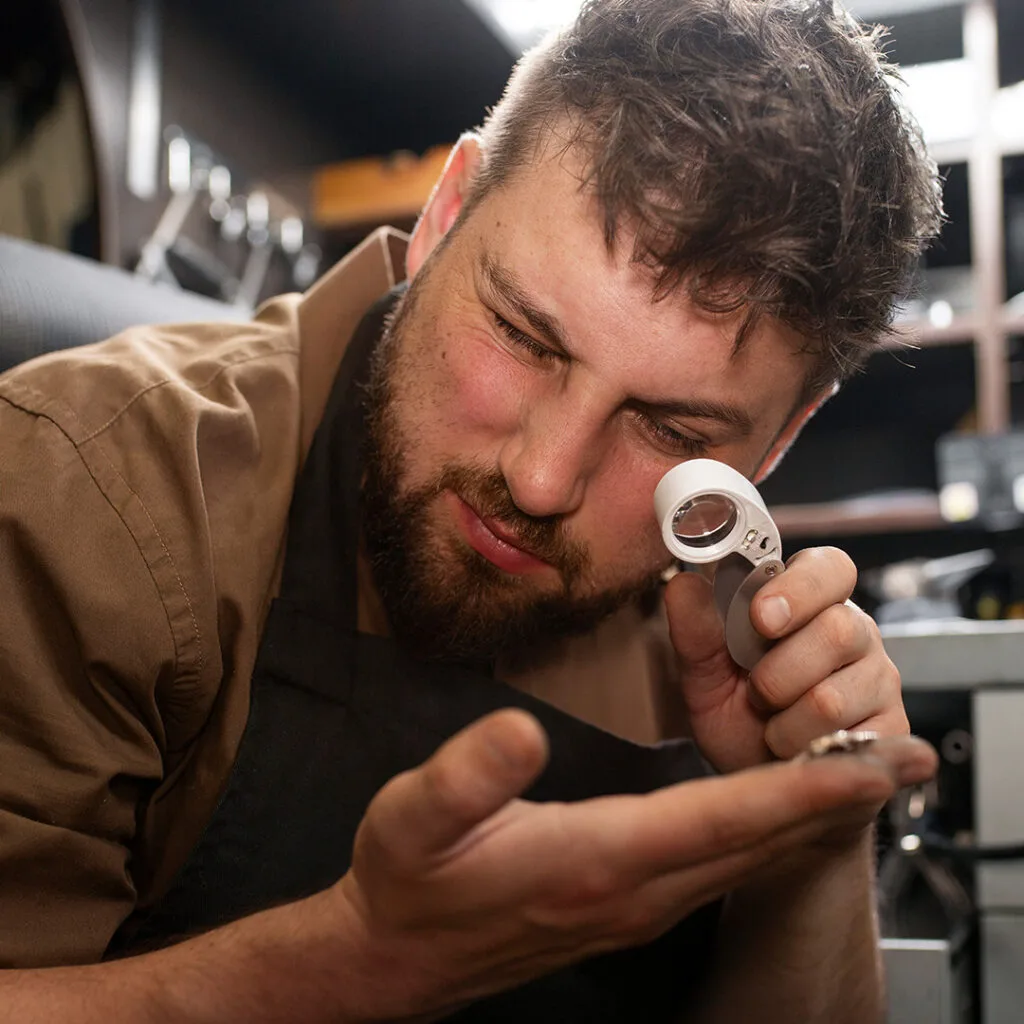 Locksmith closely inspecting a small lock component with a magnifier, ideal for emergency locksmith near me repair and precision service.