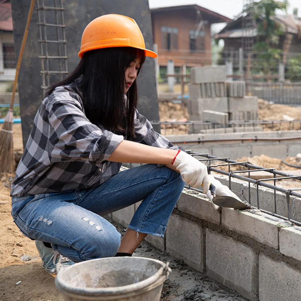 Construction worker applying mortar to a concrete block foundation at a job site, representing masonry contractors near me.