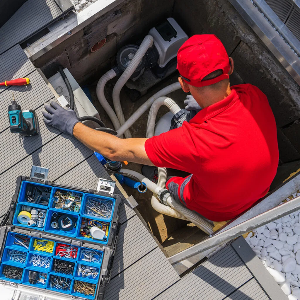 Technician in red uniform servicing pool pump system with tool kit open, suitable for a pool service near me maintenance request.