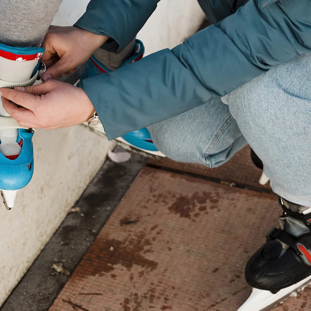 Person fastening a child’s ice skate at an outdoor rink, unrelated to mold remediation near me or home repair services.