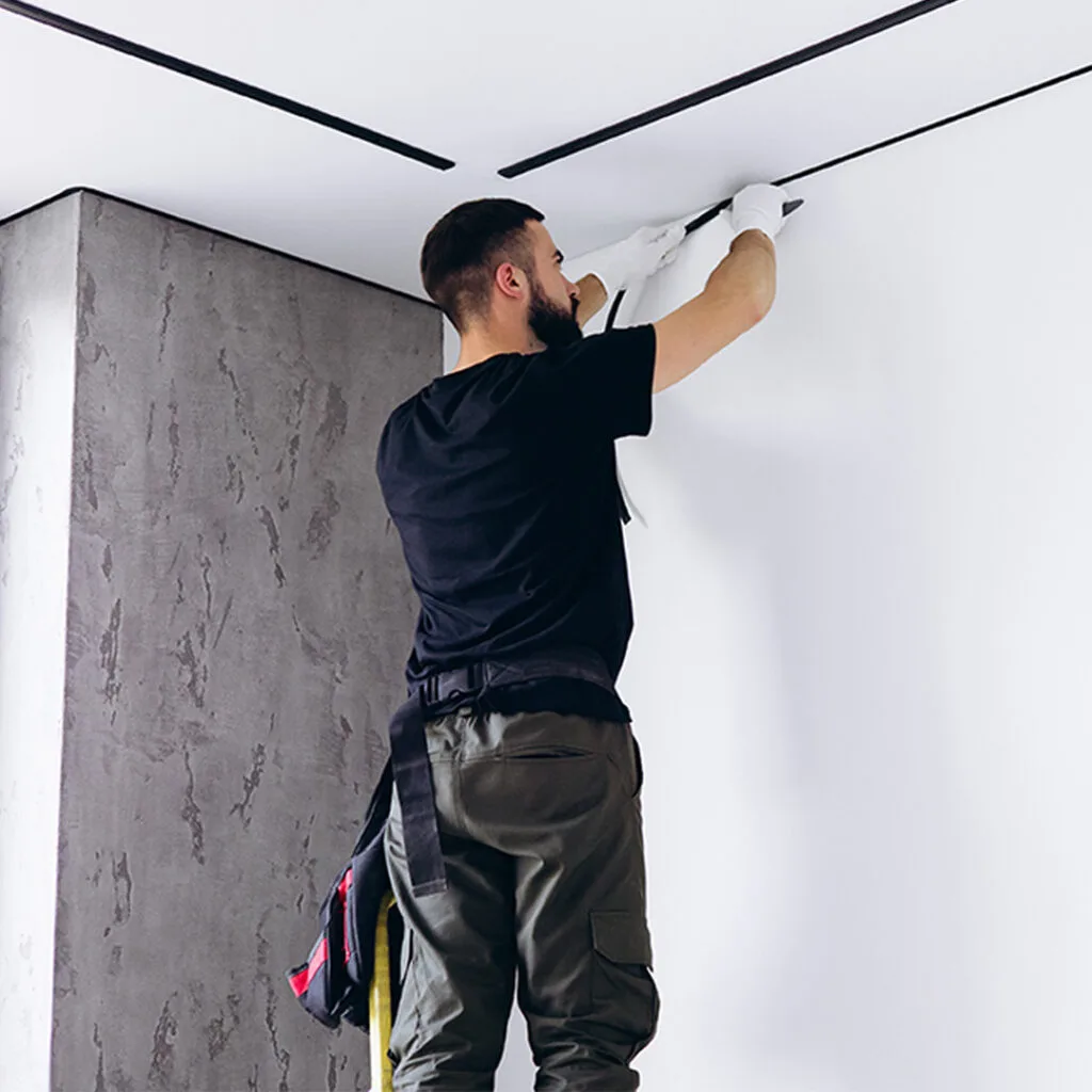 Worker installing or adjusting ceiling wiring channels during drywall repair near me service in a modern interior.