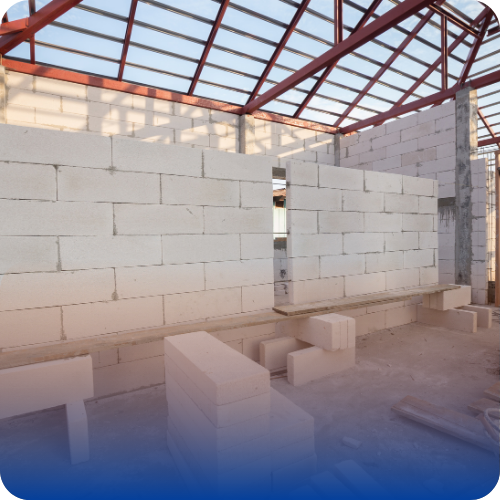Interior view of a building under construction with concrete block masonry walls and a steel roof frame.