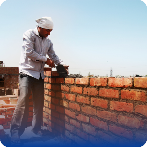 Construction worker laying bricks and applying mortar while building a brick wall outdoors.