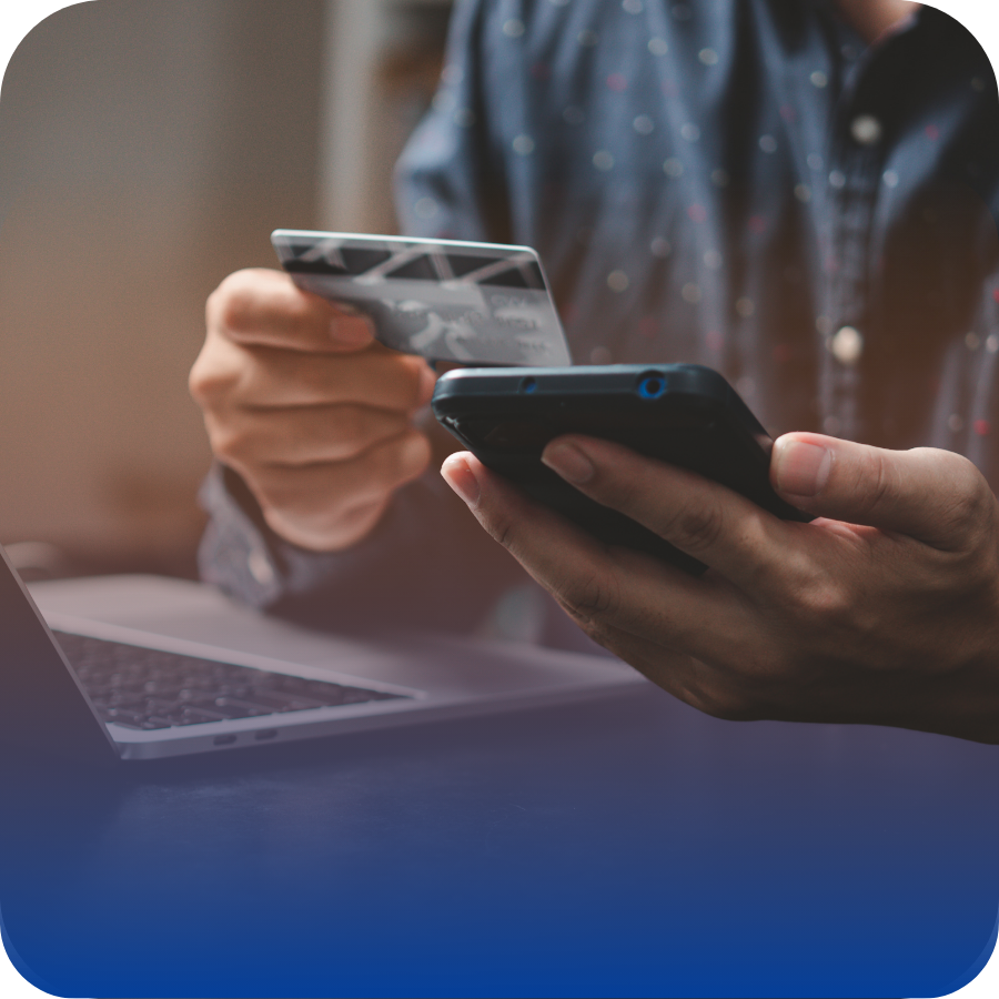 A man is holding a credit card while using a laptop, indicating an online purchase or financial transaction.