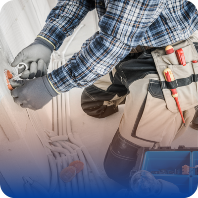 A man, dressed as a contractor, is fixing a plumbing issue under a sink with tools in hand.