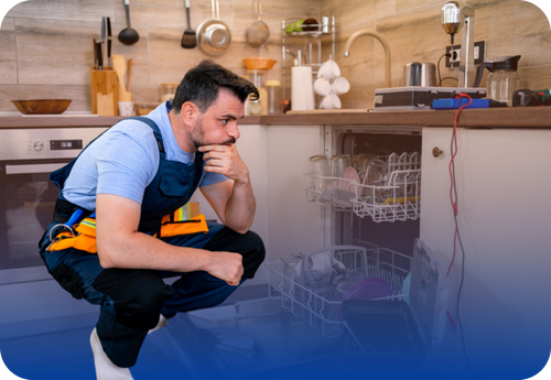 A man crouches by a dishwasher, examining it for seasonal problems related to home appliances.