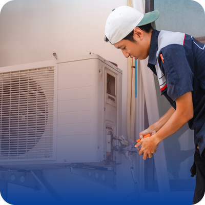 A technician in a white hat and blue shirt is fixing an air conditioner, showcasing HVAC repair services for homeowners.