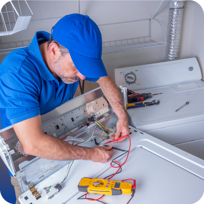 A man in a blue shirt repairs a washing machine, focusing on preventing overheating appliances for homeowners.