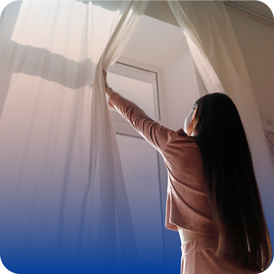 A woman opening a window curtain, highlighting the need to ventilate areas if gas or burning smells are detected.